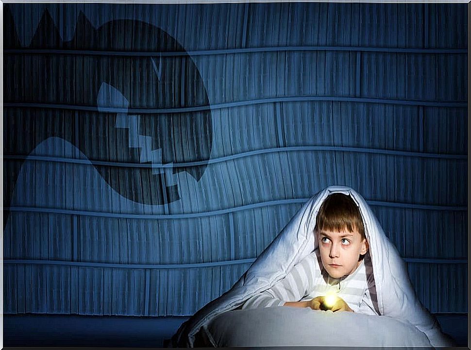 A boy in bed with a flashlight and a monster on the wall