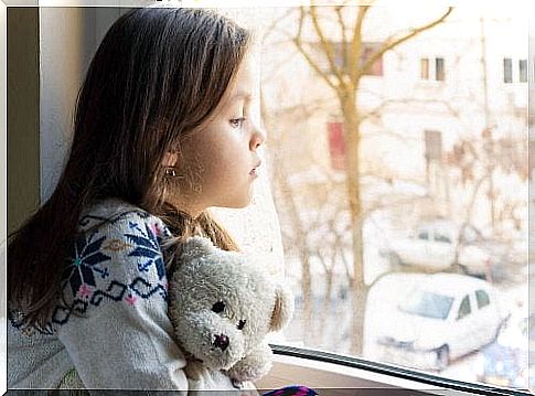 little girl with a teddy bear in the window